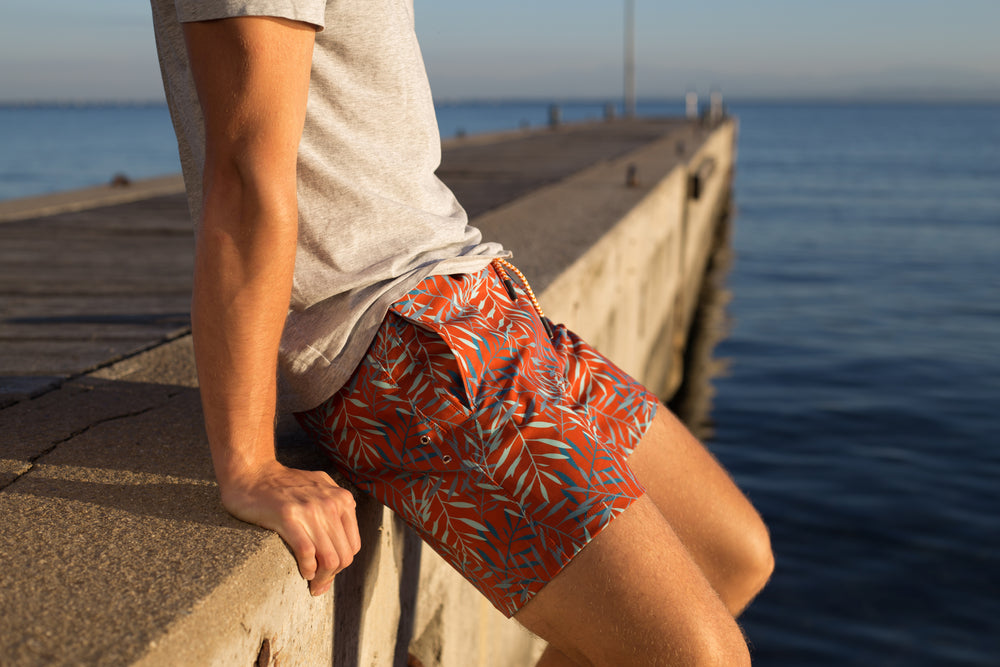 Man sitting on seaside pier in orange swim shorts
